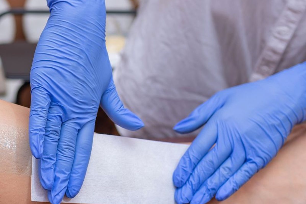 Wax strip being pressed onto the leg by a gloved therapist